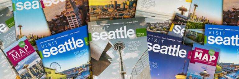 A variety of "Visit Seattle" visitor guides and Seattle maps are spread out, featuring images of the Space Needle, Seattle’s skyline, and waterfront attractions on their colorful covers.