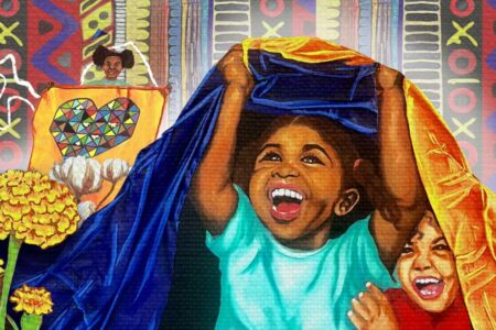 Two smiling children play under a brightly colored blanket fort, while another child in the background holds up a quilt with a patterned heart. The scene is vibrant with bold patterns and flowers surrounding the children.