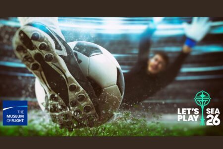 A close-up of a soccer player's cleat kicking a ball toward the goal as a goalkeeper dives to block it. Logos for The Museum of Flight and 
