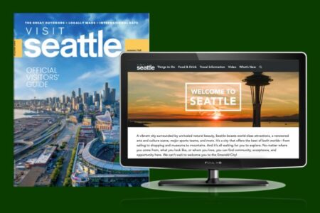 A Seattle visitor's guide magazine featuring a cityscape is displayed next to a computer monitor showing a 
