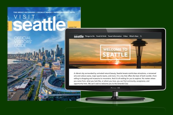 A Seattle visitor's guide magazine featuring a cityscape is displayed next to a computer monitor showing a "Welcome to Seattle" webpage with a sunset and space needle image.