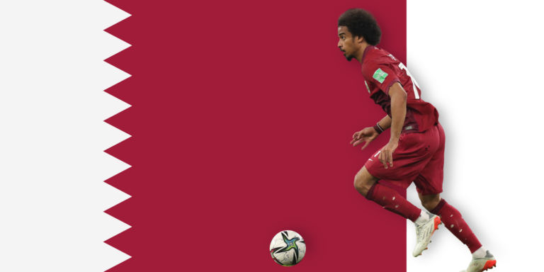 A soccer player in a maroon uniform runs towards a ball on a background resembling the Qatar flag, featuring a maroon field with a white serrated band.