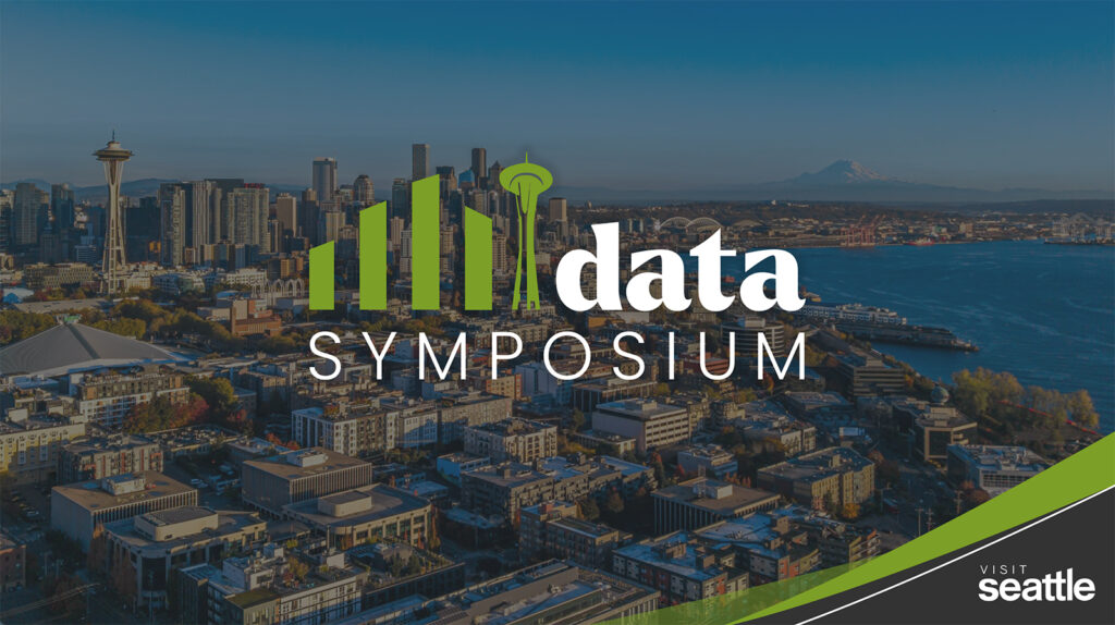 Aerial view of downtown Seattle with the Space Needle, mountain in the distance, and waterfront. Overlay text reads "Data Symposium" with a green bar graph and Space Needle icon; "Visit Seattle" in the corner.