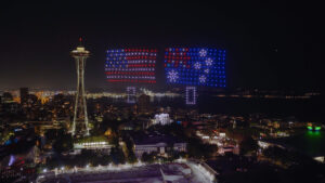A nighttime view of Seattle with the Space Needle, where a drone light display shows the American and Australian flags above the cityscape, as Seattle names VP of meetings and conventions.