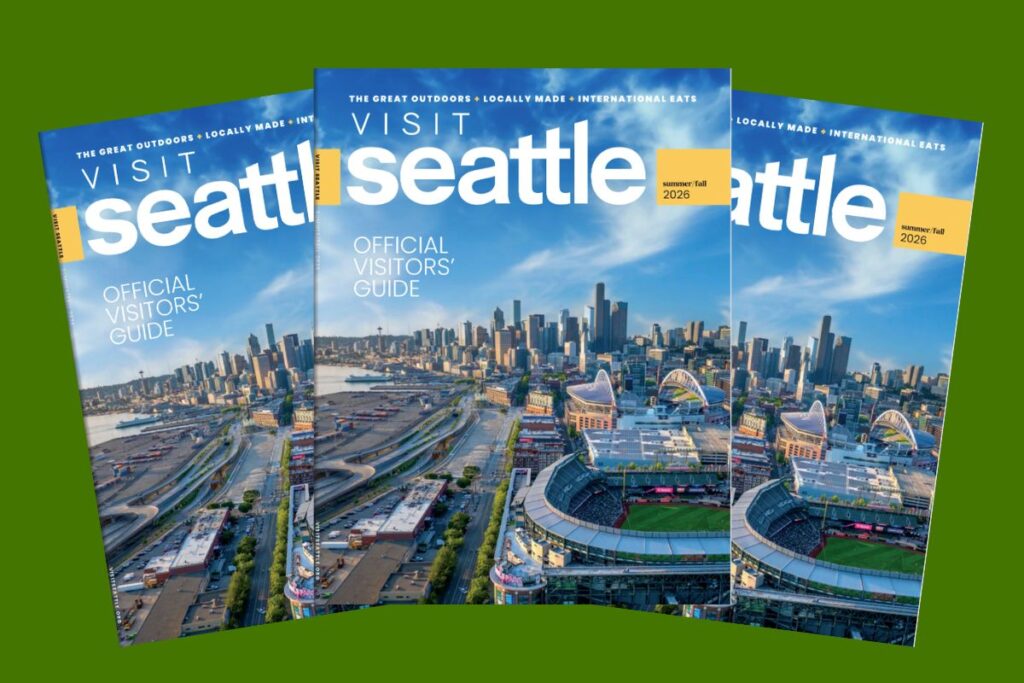 Three copies of the “Visit Seattle Official Visitors’ Guide” magazine, featuring an aerial view of downtown Seattle and a stadium on the cover, displayed against a green background.