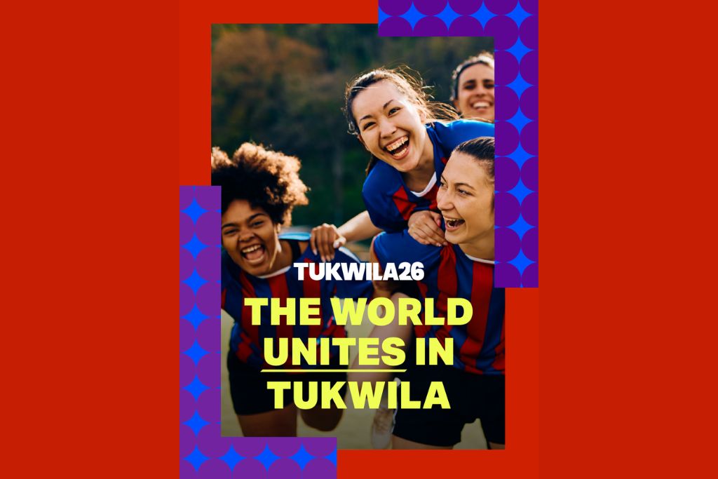 Four smiling people in soccer jerseys huddle together outdoors. Bold text on the image reads: “TUKWILA26. THE WORLD UNITES IN TUKWILA.” The design features blue and purple geometric patterns and a red background.