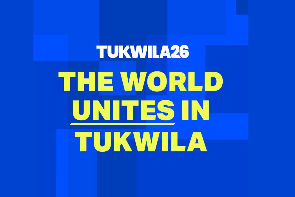 White text at the top reads "TUKWILA26." Below, bold yellow text says "THE WORLD UNITES IN TUKWILA" on a blue background with various blue rectangles.