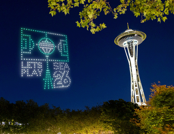 A group of drones forms the 2026 FIFA World Cup logo in green and white lights near Seattle’s Space Needle at night, with trees and a dark blue sky in the background.