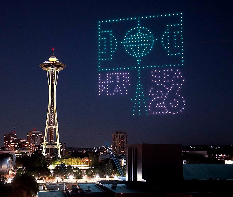 Colorful drones form the 2026 FIFA World Cup logo in the night sky near Seattle’s Space Needle, with city lights visible below.