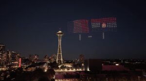 The Space Needle in Seattle at night is illuminated by a mesmerizing drone light show above, with a vibrant drone scoreboard displaying two soccer team flags and the score “1-1” in the sky—an unforgettable spectacle for anyone planning to Visit Seattle during the FIFA World Cup.