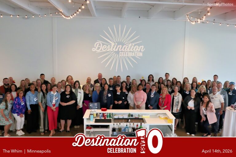 A large group of people pose, smiling, in front of a white wall with a "Destination Celebration" logo. They stand around a bar in a bright event space, with string lights above. Event branding and date appear at the bottom.