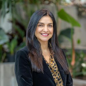 A woman with long dark hair smiles while wearing a black blazer and a leopard-print top.